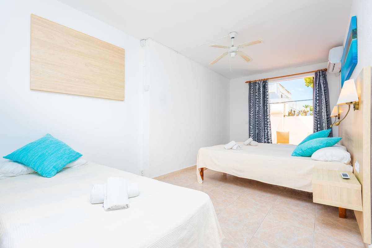 A hotel room with two beds, a ceiling fan, a window with curtains, and a nightstand with a lamp.