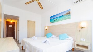 Een hotelkamer met een bed, een bureau, een schilderij van een strand en een plafondventilator.