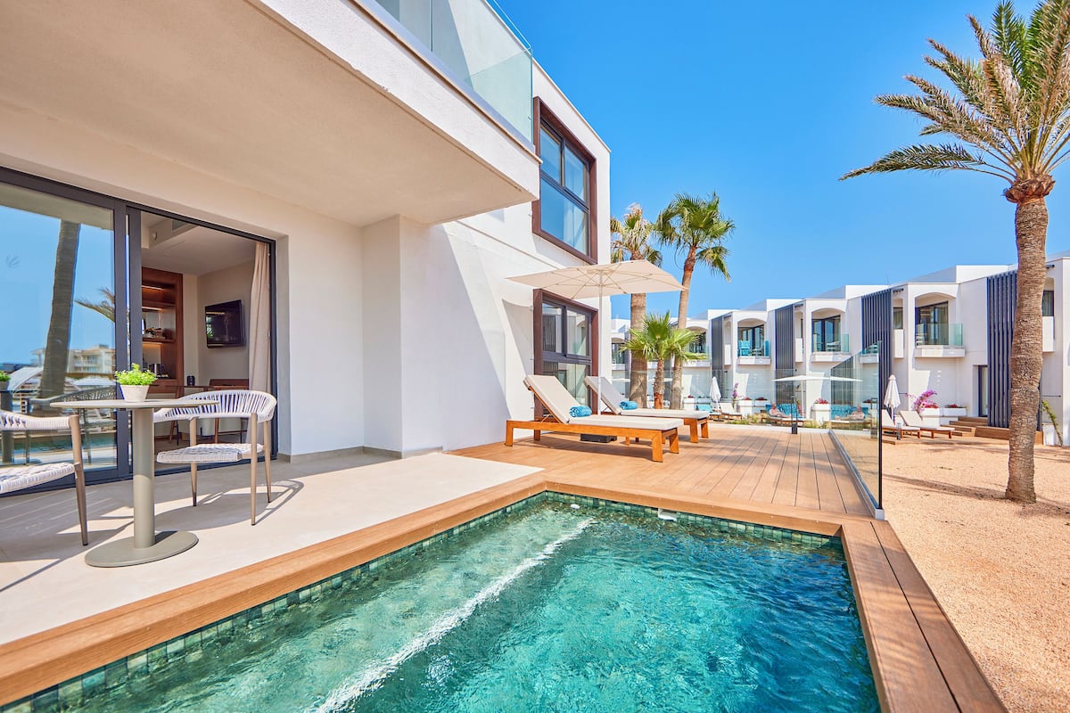 A modern pool area with a clear pool, lounge chairs, and a table with chairs.