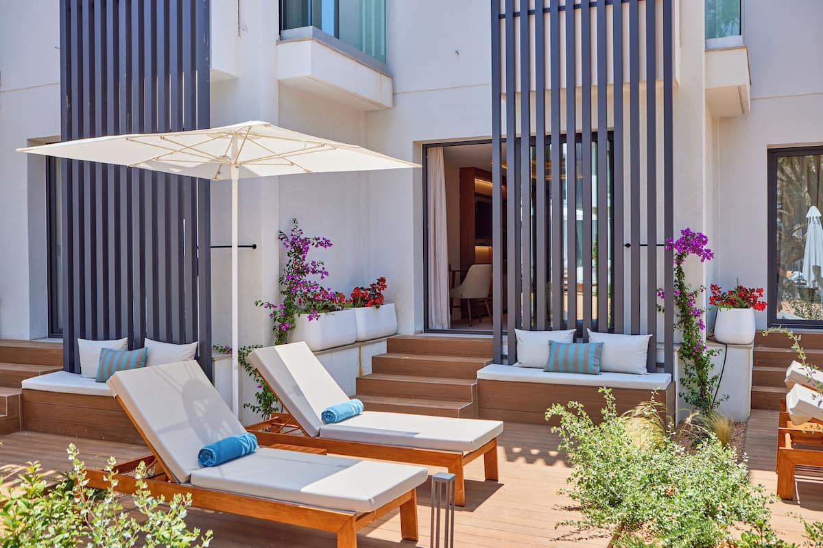 A modern outdoor seating area with lounge chairs and a large umbrella, surrounded by potted plants and flowers.