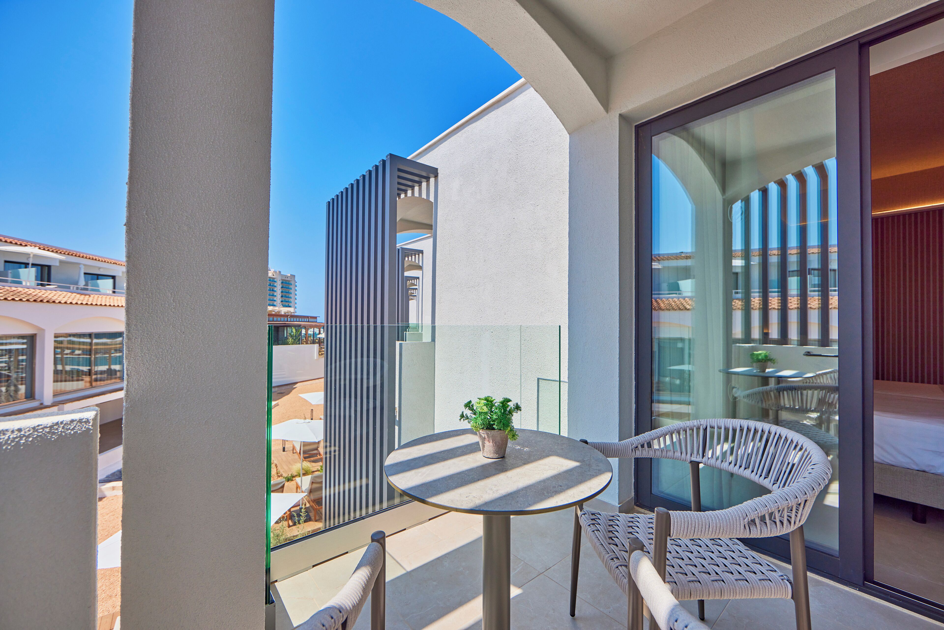 A balcony with a round table and two wicker chairs, a potted plant, and a view of the cityscape.