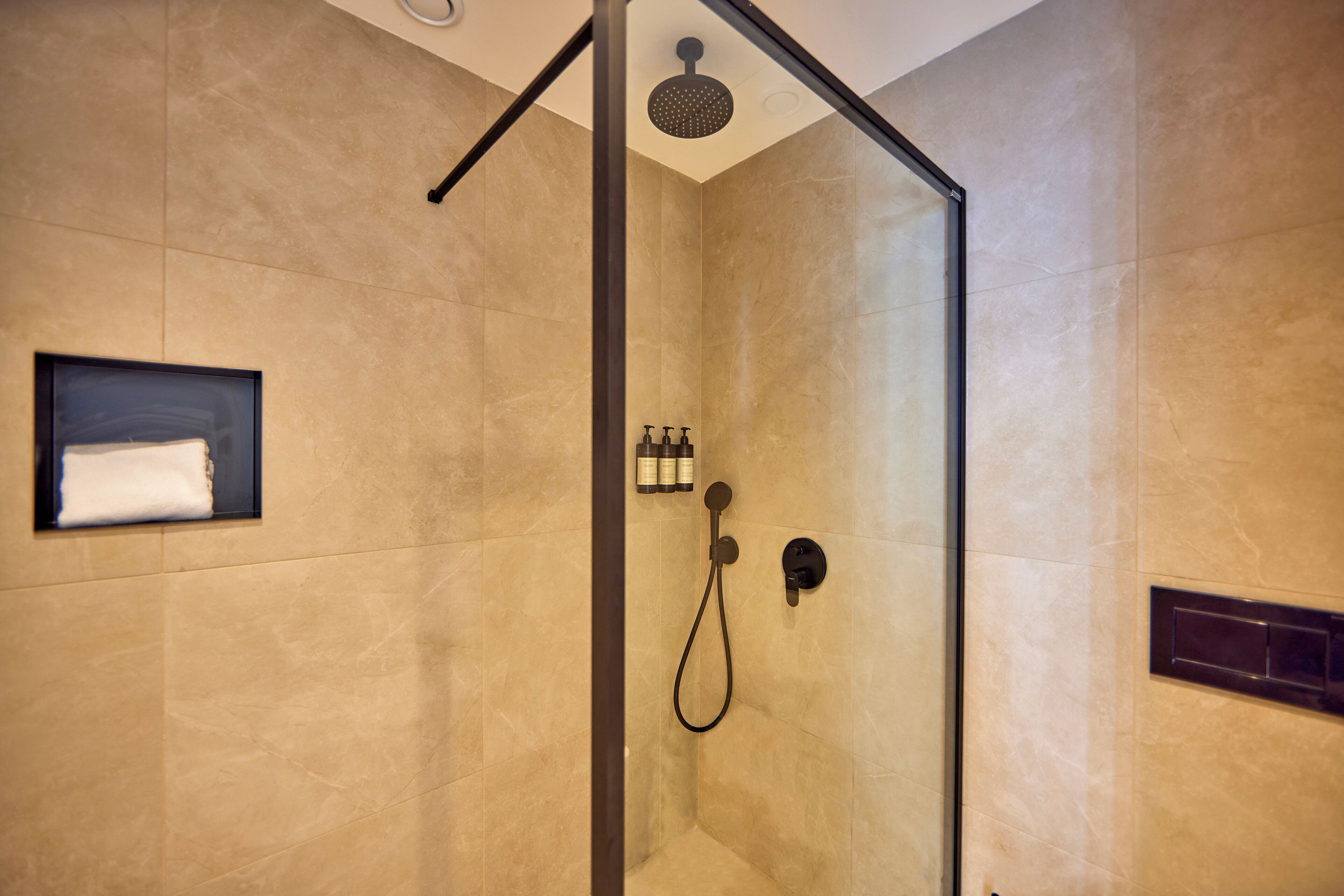 Eine begehbare Dusche mit Glastrennwand, einer Handbrause, einem fest installierten Bedienfeld und einem gerahmten Bild an der Wand.