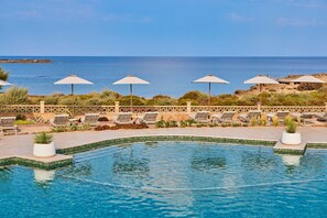A pool area with lounge chairs and umbrellas, a clear view of the sea, and a tiled edge. - Universal Grand León & Spa (Ses Salines)