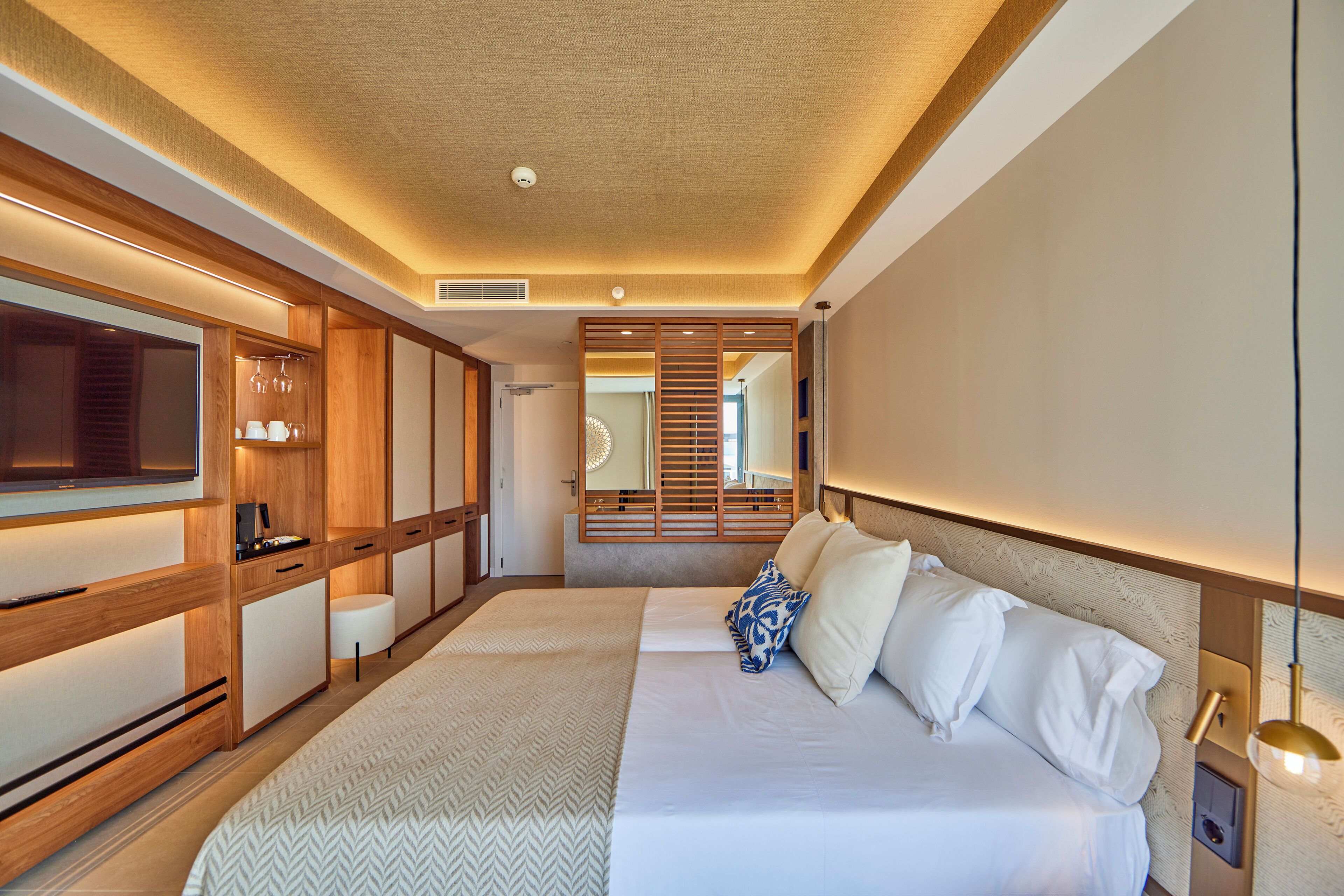 Quarto de hotel moderno com uma cama grande, televisão integrada e uma porta de madeira deslizante para um banheiro.