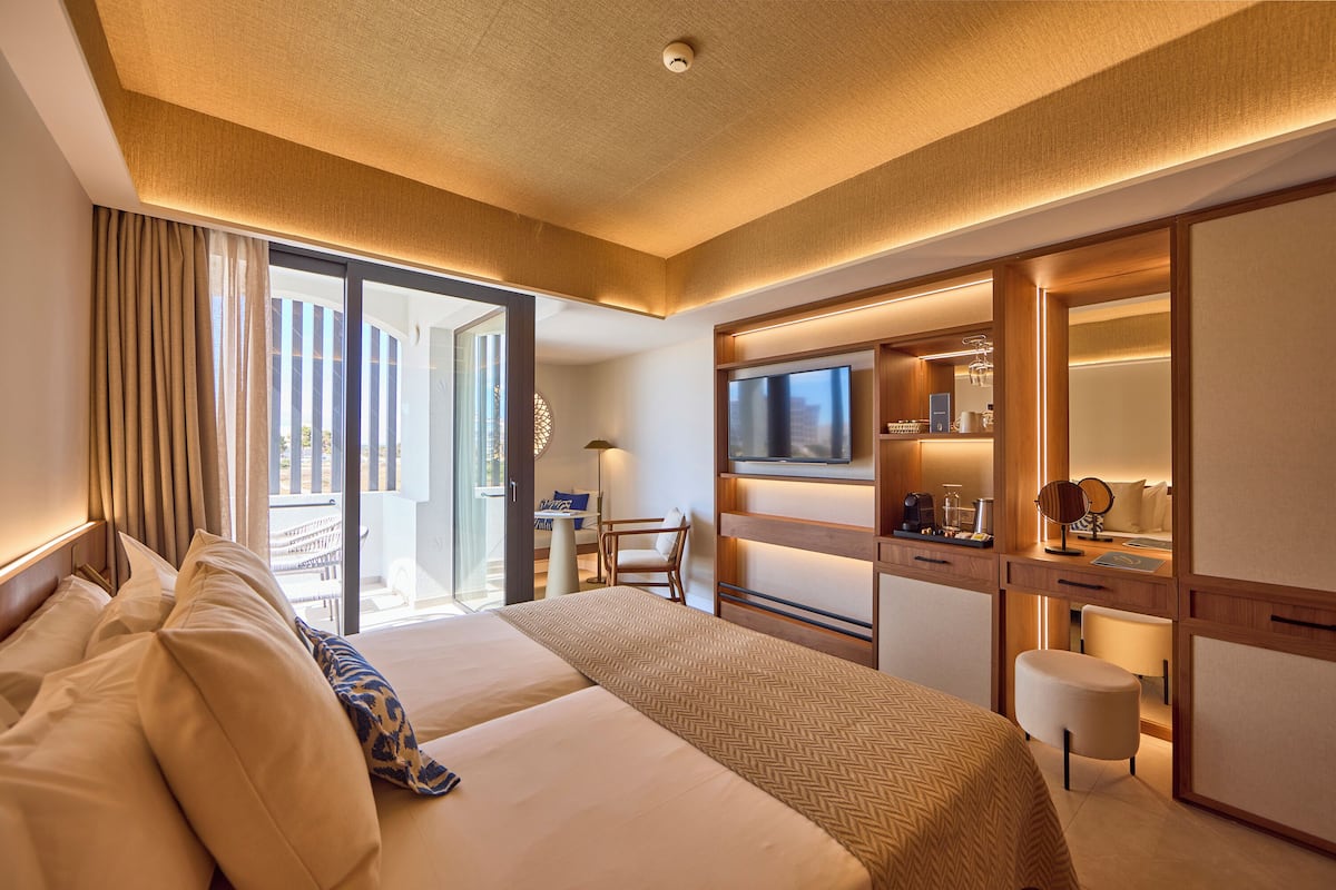 A hotel room with a large bed, a TV, a desk with a chair, and a sliding glass door to the balcony.