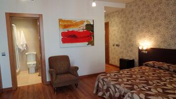 Een hotelkamer met een bed, een stoel, een toilet en een schilderij aan de muur.