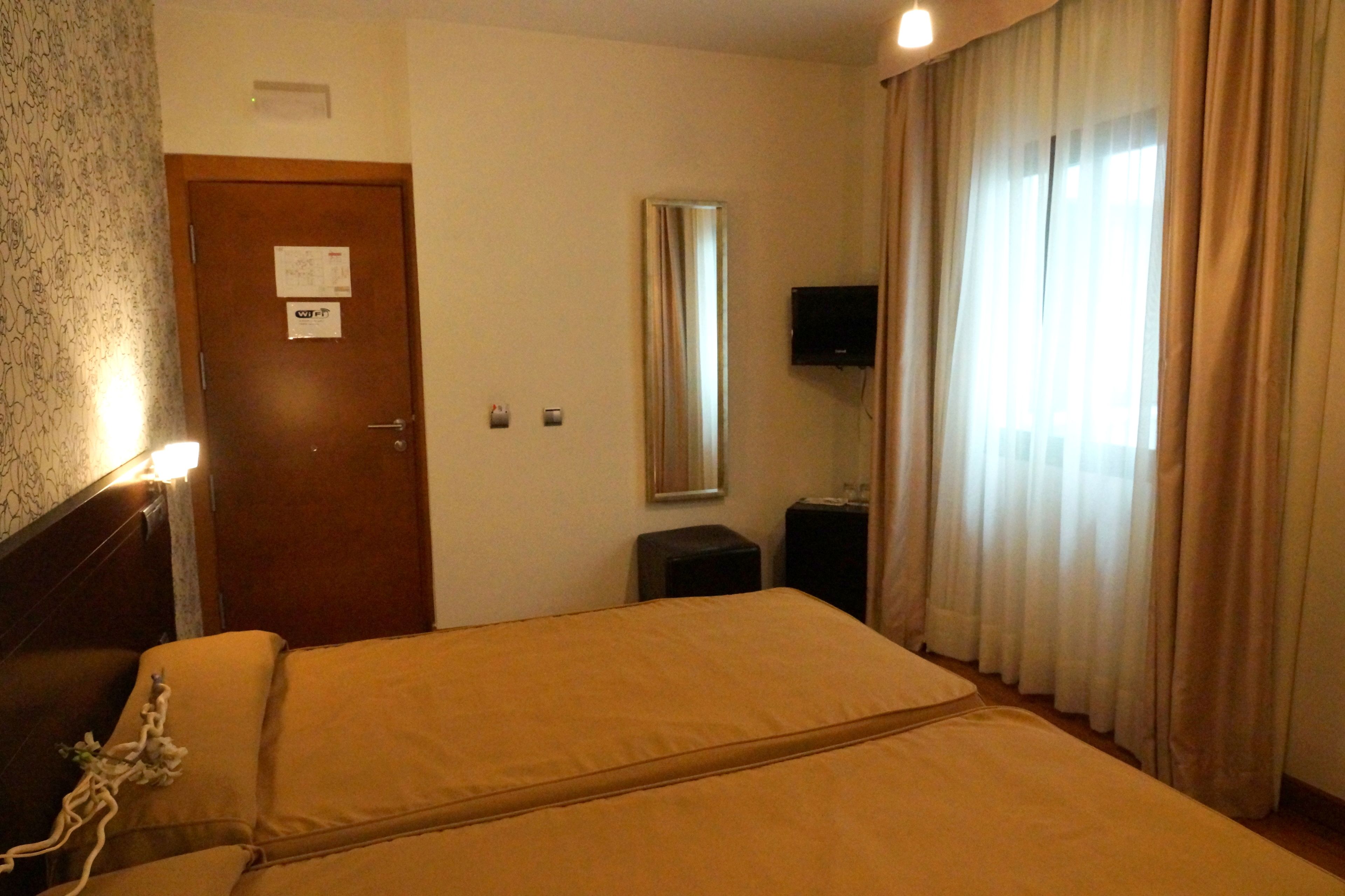 A hotel room with a bed, a television, a door with a sign, and a window with curtains.