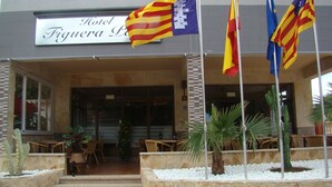 A hotel entrance with a sign reading "Hotel Figuera Lo". There are flags, outdoor seating, and a stone staircase leading to the entrance. - Residencia Santiago Mallorca (Santanyi)