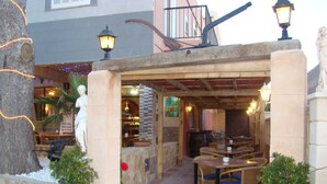 An outdoor patio area with stone pillars, wooden tables and chairs, potted plants, and a statue. - Residencia Santiago Mallorca (Santanyi)