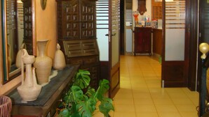 A dining area with a wooden table, chairs, and a large potted plant. There is a mirror on the wall and a chandelier above. - Residencia Santiago Mallorca (Santanyi)