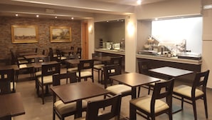 Un restaurant amb taules i cadires de fusta, una paret de rajola amb quadres emmarcados i un taulell ple d'aliments i begudes.