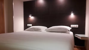 Habitació d'hotel moderna amb un llit gran, dues taules de nit i il·luminació penjada a la paret.