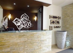 A reception area with a stone counter, abstract wall art, framed fish pictures, and a large planter. - Hotel Bocage (Setubal)