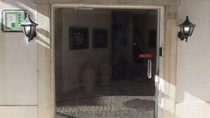 A hotel entrance with a glass door, two wall-mounted lamps, and a tiled floor. - Guest House Bocage (Setubal)