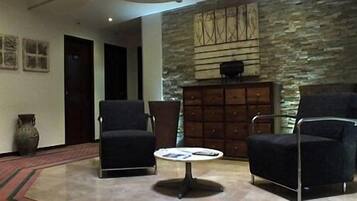 A lobby with two armchairs, a coffee table, a stone wall with a decorative panel, and a wooden cabinet.