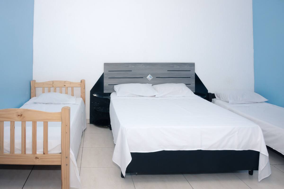 Un dormitorio con dos camas, una de madera y otra con estructura negra, frente a una pared azul y blanca.