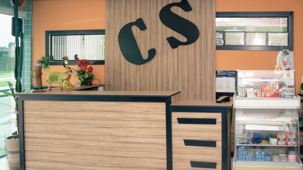 Una recepción con detalles de madera y acentos negros, un letrero grande con las letras 'CS' arriba y un expositor refrigerado a la derecha.