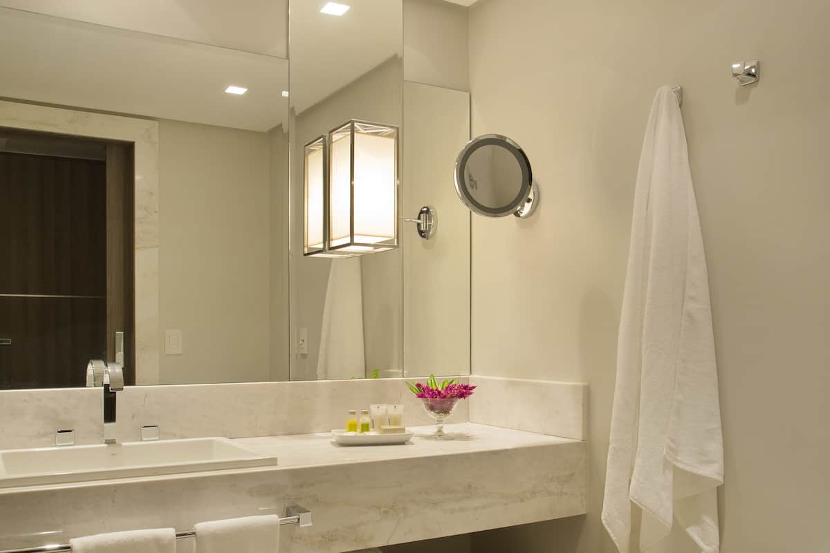 A modern bathroom with a large mirror, a sink, and a toilet. There are towels and a small shelf with toiletries.