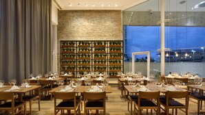 Um restaurante com várias mesas preparadas para refeições, uma parede de tijolos e uma grande janela com vista para a paisagem urbana.