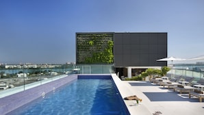 Piscina no terraço com barreira de vidro, cadeiras de lounge e vista para a cidade.
