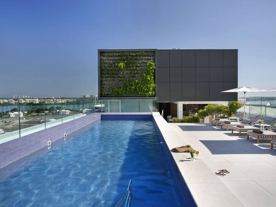 Piscina no terraço com barreira de vidro, cadeiras de lounge e vista para a cidade.