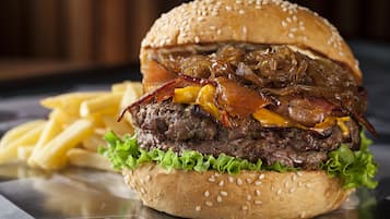 A burger with lettuce, cheese, and bacon on a sesame seed bun, accompanied by French fries.