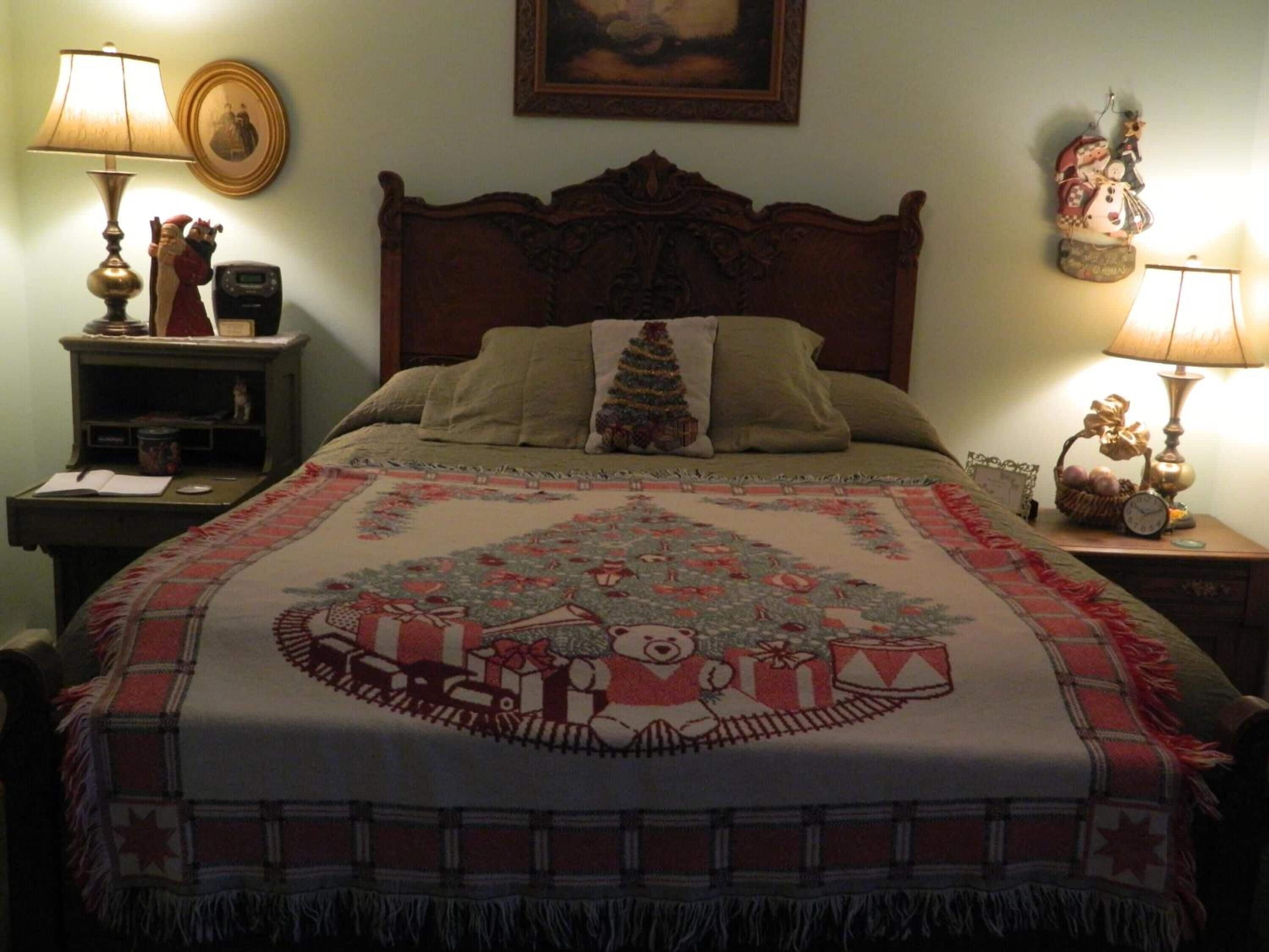 Ein Schlafzimmer mit einem hölzernen Kopfteil, einer weihnachtlichen Bettdecke, zwei Nachttischen mit Lampen, einem Beistelltisch und einer an der Wand befestigten Uhr.