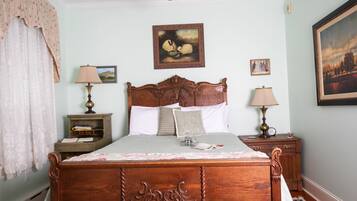 A traditional bedroom with a wooden bed, two bedside tables with lamps, a ceiling fan, and framed artwork on the walls.