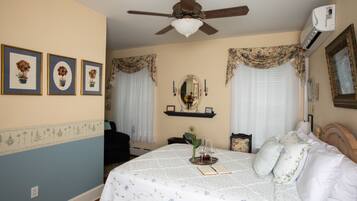A bedroom with a bed, a ceiling fan, an air conditioner, a framed mirror, and a shelf with decorative items.