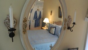 A bedroom with a bed, a nightstand, a lamp, a robe, and a mirror with decorative elements. - E J Bowman House Bed & Breakfast (Lancaster)