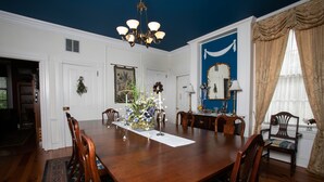 A formal dining room with a large wooden table, chairs, a chandelier, and a blue accent wall. - E J Bowman House Bed & Breakfast (Lancaster)