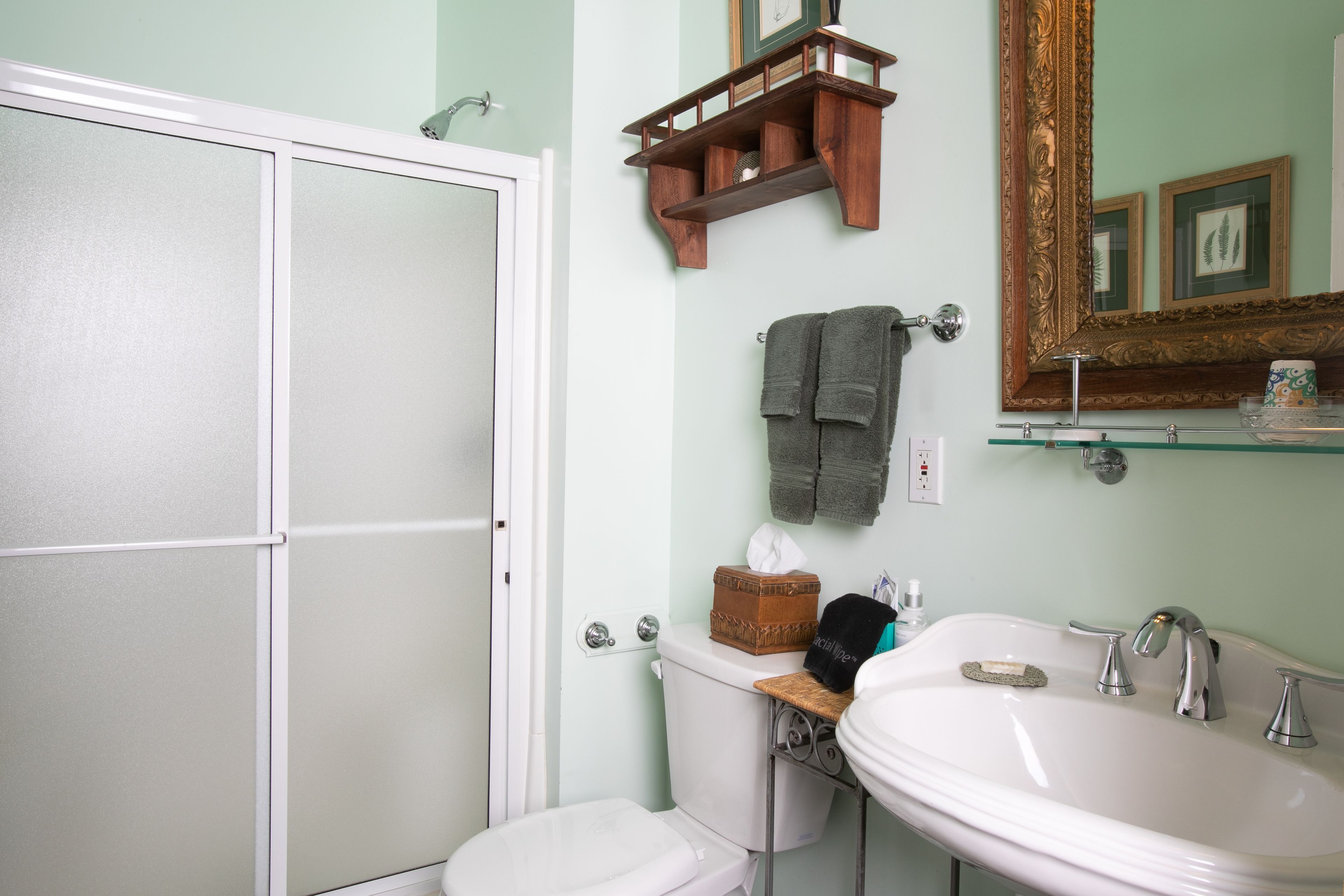A bathroom with a toilet, sink, and mirror. There is a towel rack with towels and a small shelf with toiletries.