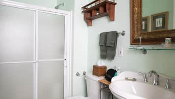 A bathroom with a toilet, sink, and mirror. There is a towel rack with towels and a small shelf with toiletries.