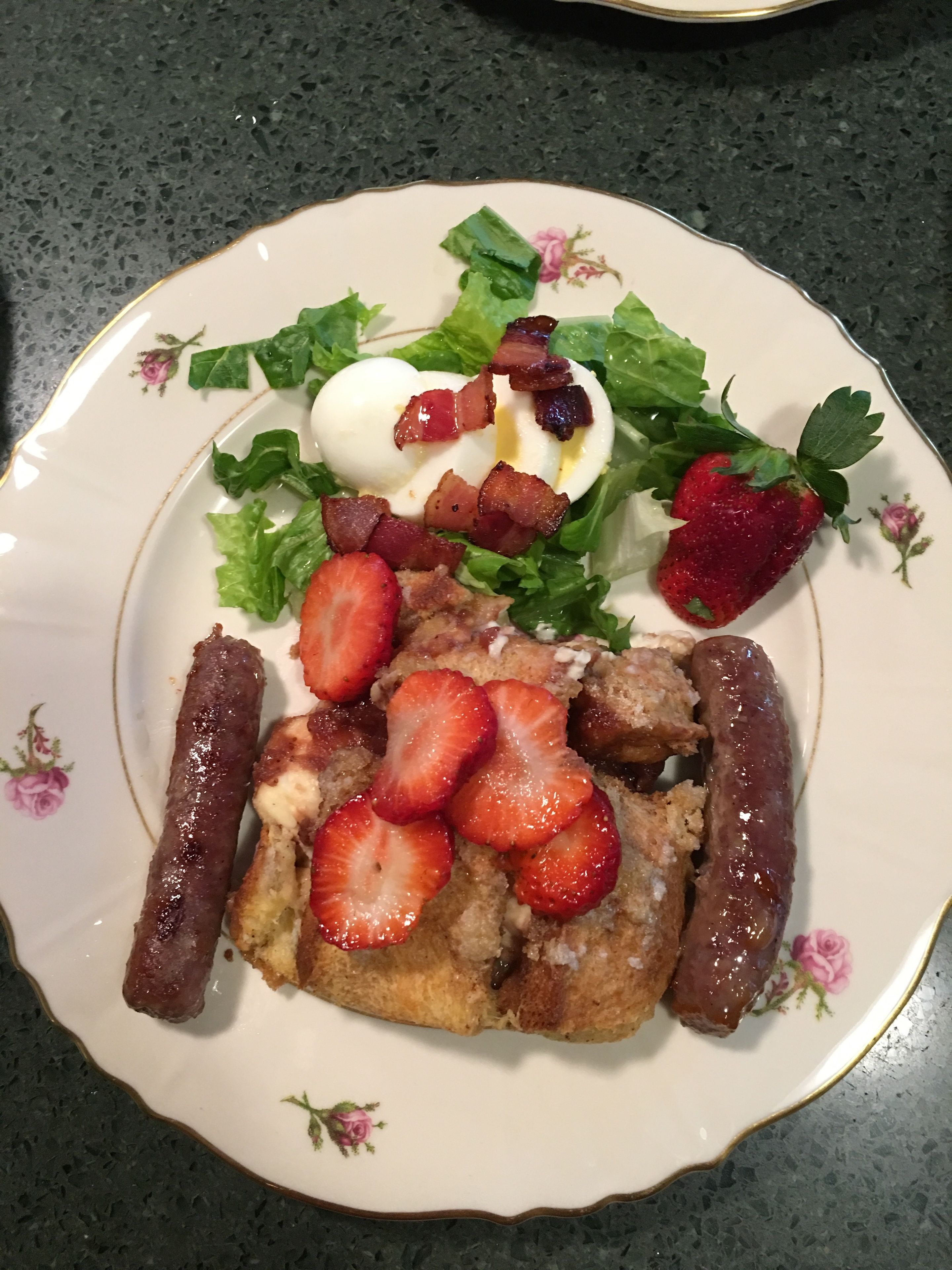 Ein Teller mit Salat, Eiern, Speck, Erdbeeren und Würstchen.