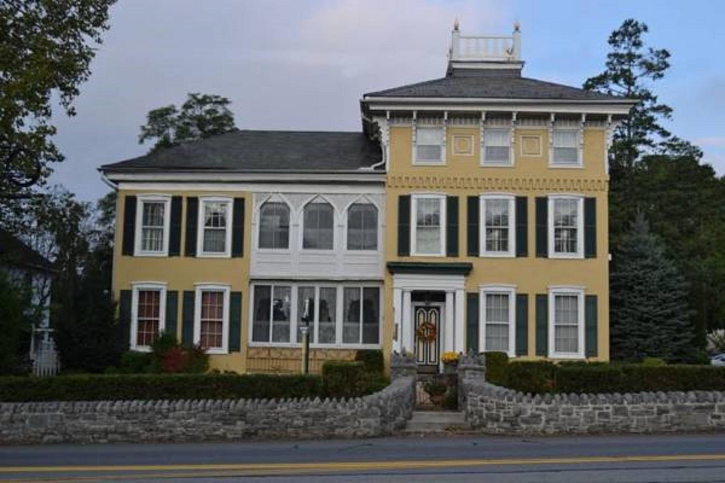 A two-story building with a yellow facade, white trim, and green shutters.