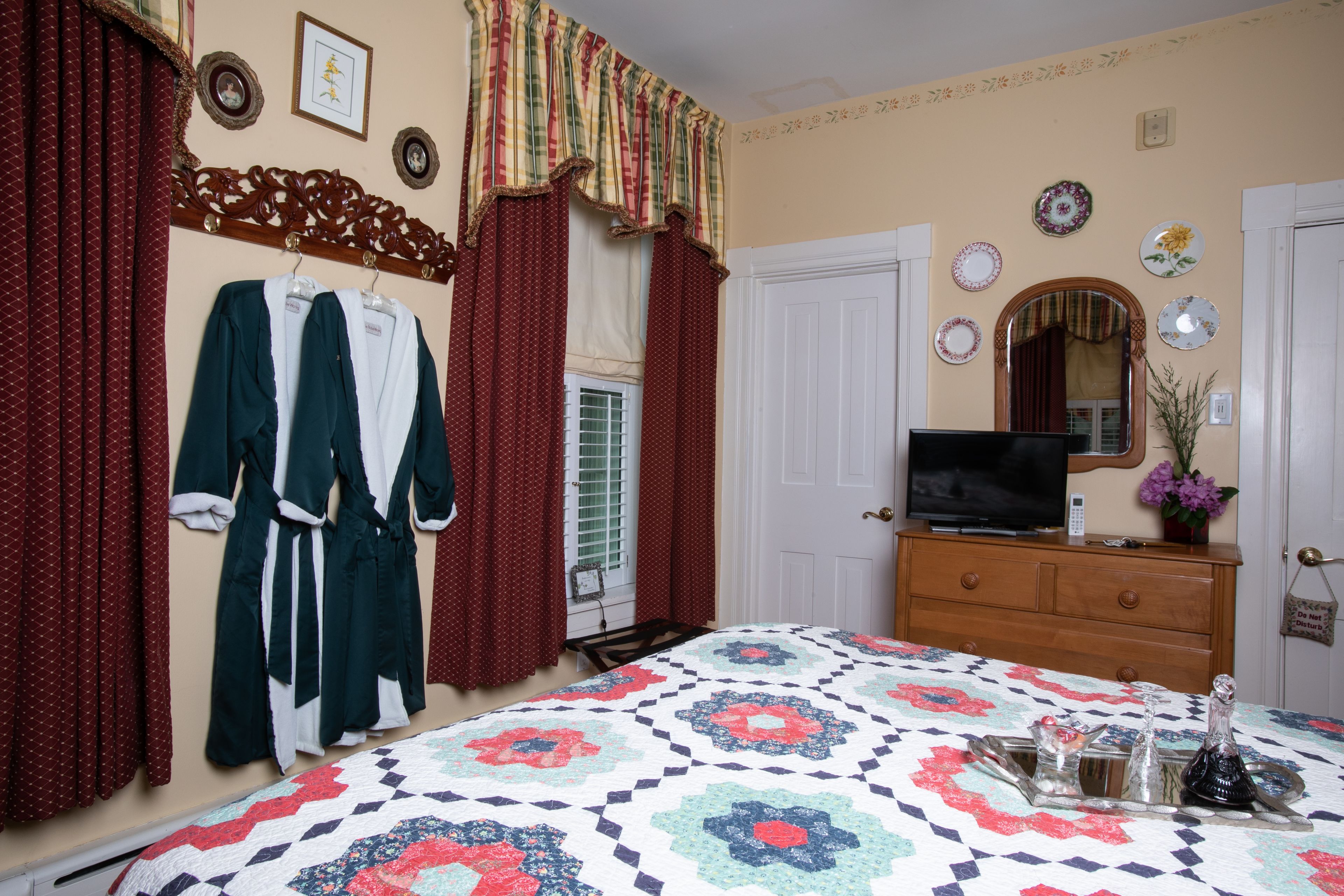 A bedroom with a bed, a dresser, a television, and a window with curtains.