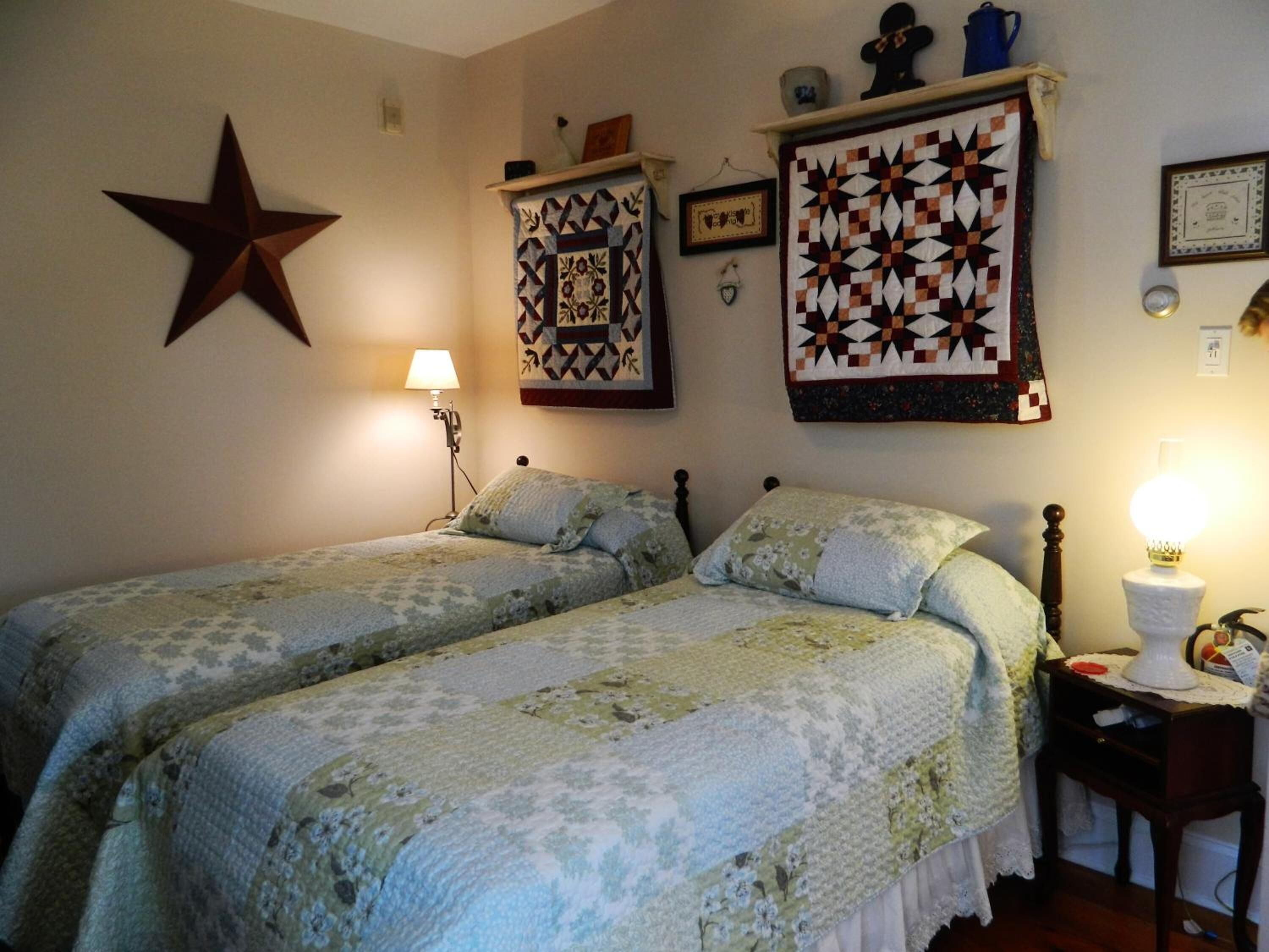 A bedroom with two beds, a star decoration, and quilts on the wall.