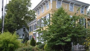 A yellow building with white trim and multiple windows, surrounded by greenery and a stone wall. - E J Bowman House Bed & Breakfast (Lancaster)