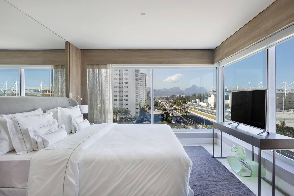 Quarto de hotel moderno com uma cama grande, uma TV e uma varanda com vista para a cidade.