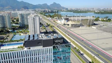 A modern hotel with a rooftop pool, a view of a busy road, and mountains in the background.