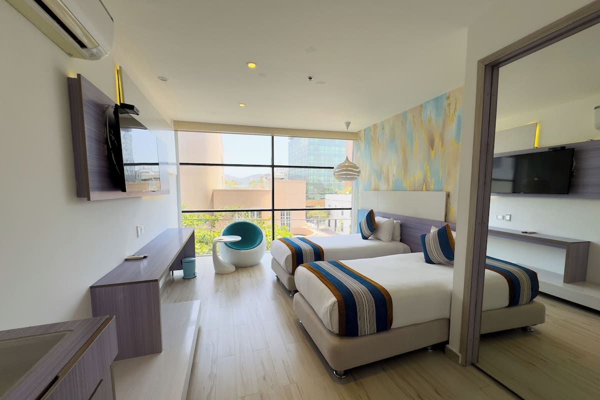 Een moderne hotelkamer met twee bedden, een bureau, een stoel en een groot raam met uitzicht op de stad.