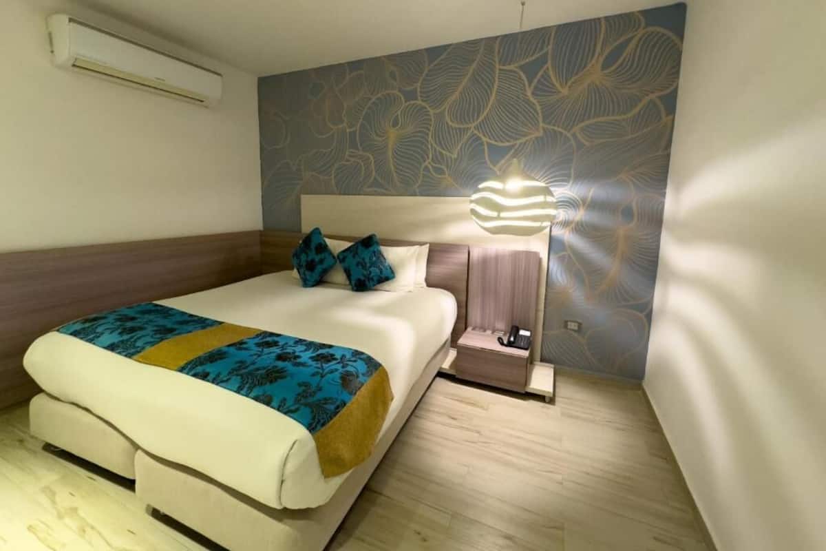 Een hotelkamer met een bed, nachtkastje, lamp en een muur met een bladpatroon.