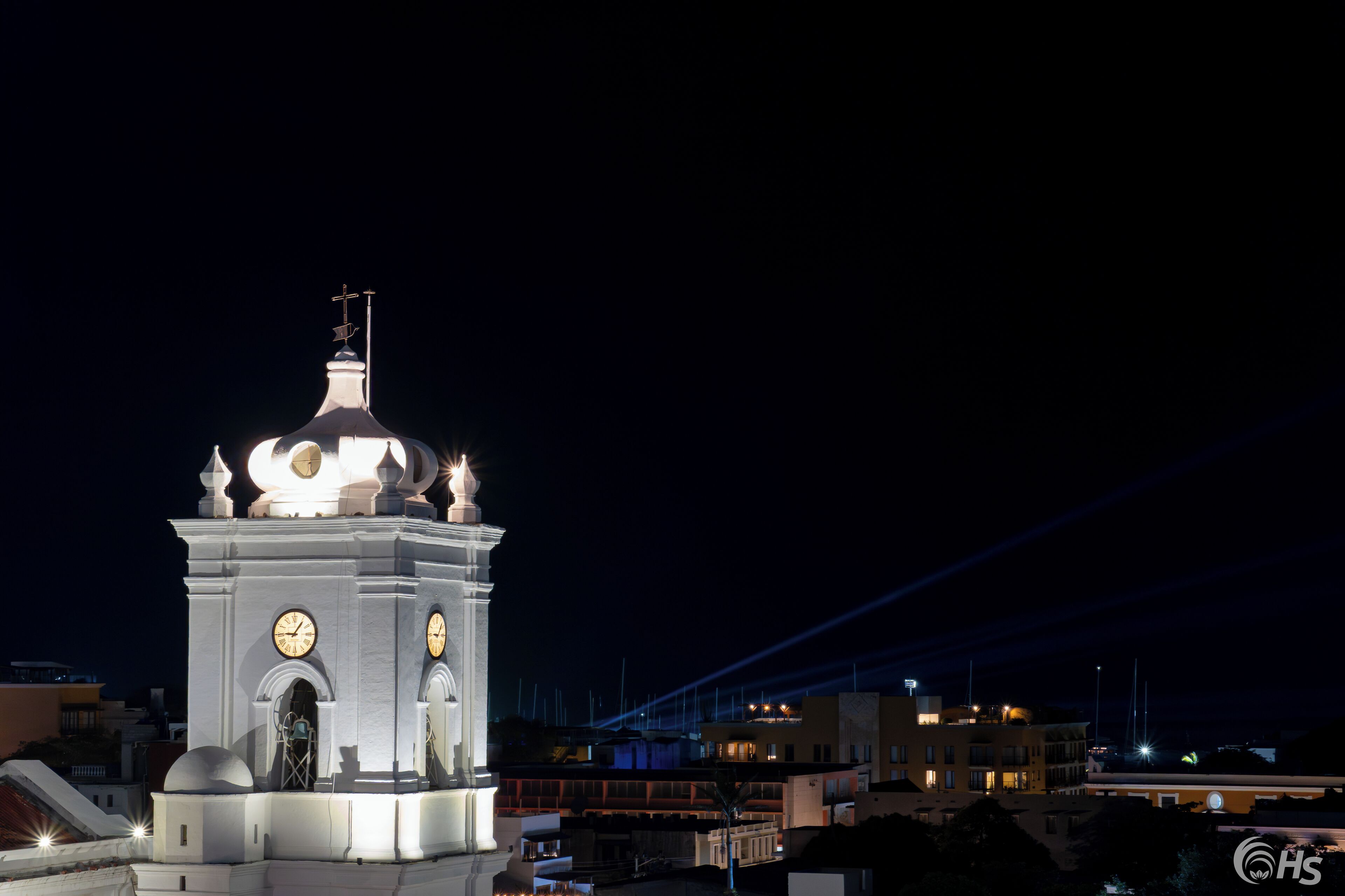 Una torre del reloj blanca con cúpula y cruz en la parte superior, rodeada de edificios.