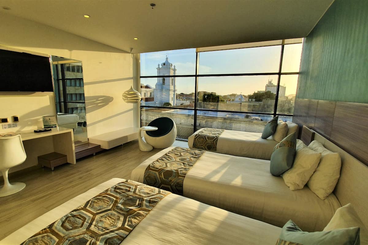 Een moderne hotelkamer met twee bedden, een bureau, een stoel en een groot raam met uitzicht op de stad.