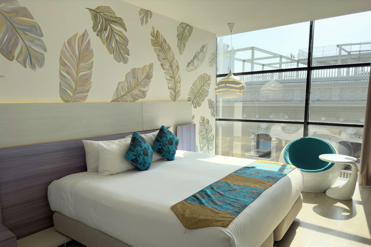 Een moderne hotelkamer met een groot bed, uitzicht op de stad door grote ramen en een balkon met een leuning.