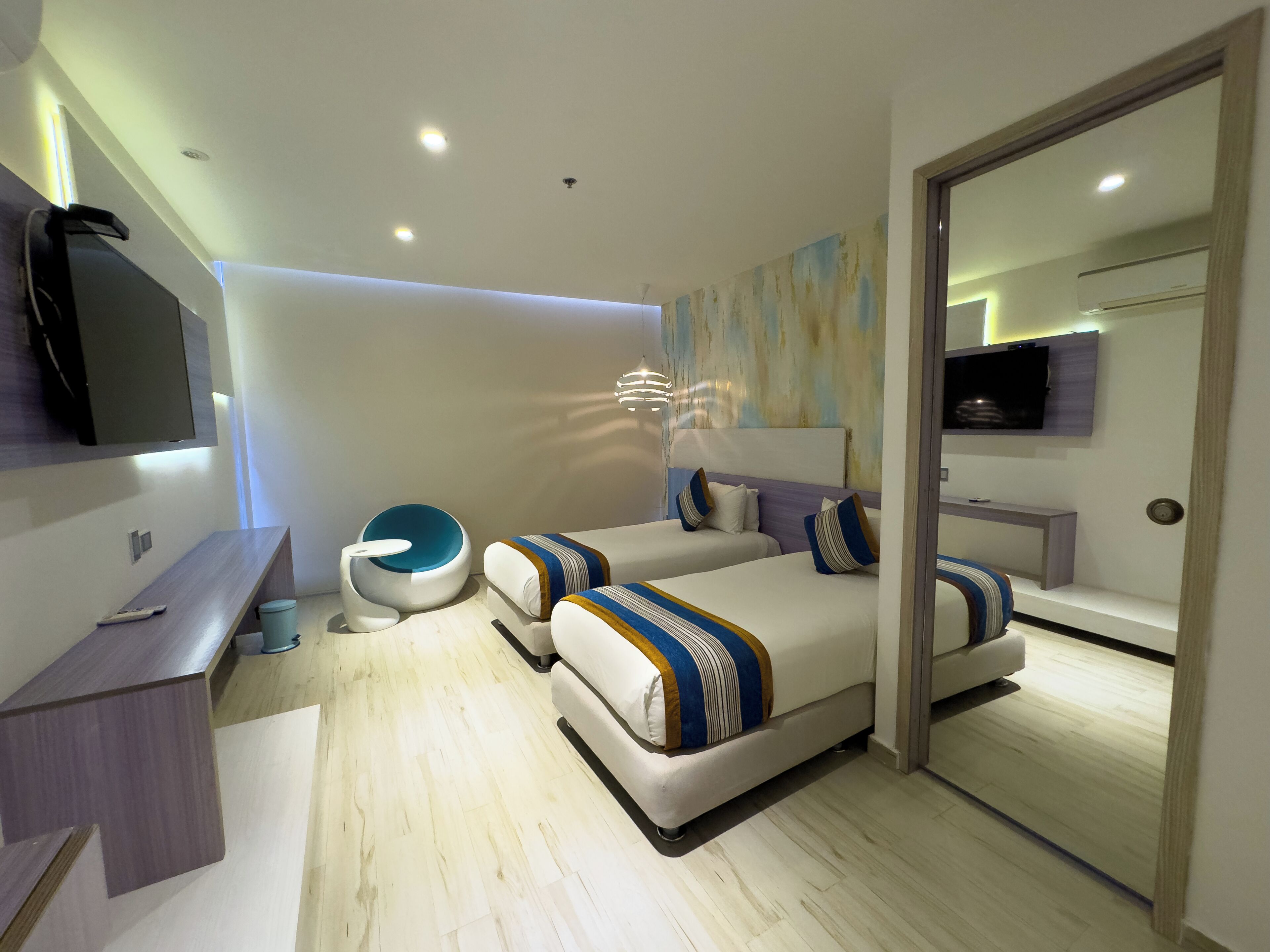 Un dormitorio moderno con dos camas, televisión, escritorio y baño.