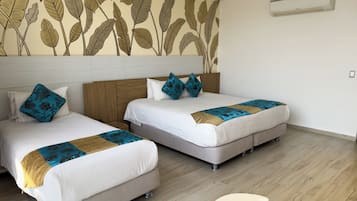Habitación de hotel con dos camas, cabecera de madera, un mural en la pared, un equipo de aire acondicionado y una pequeña mesa redonda.
