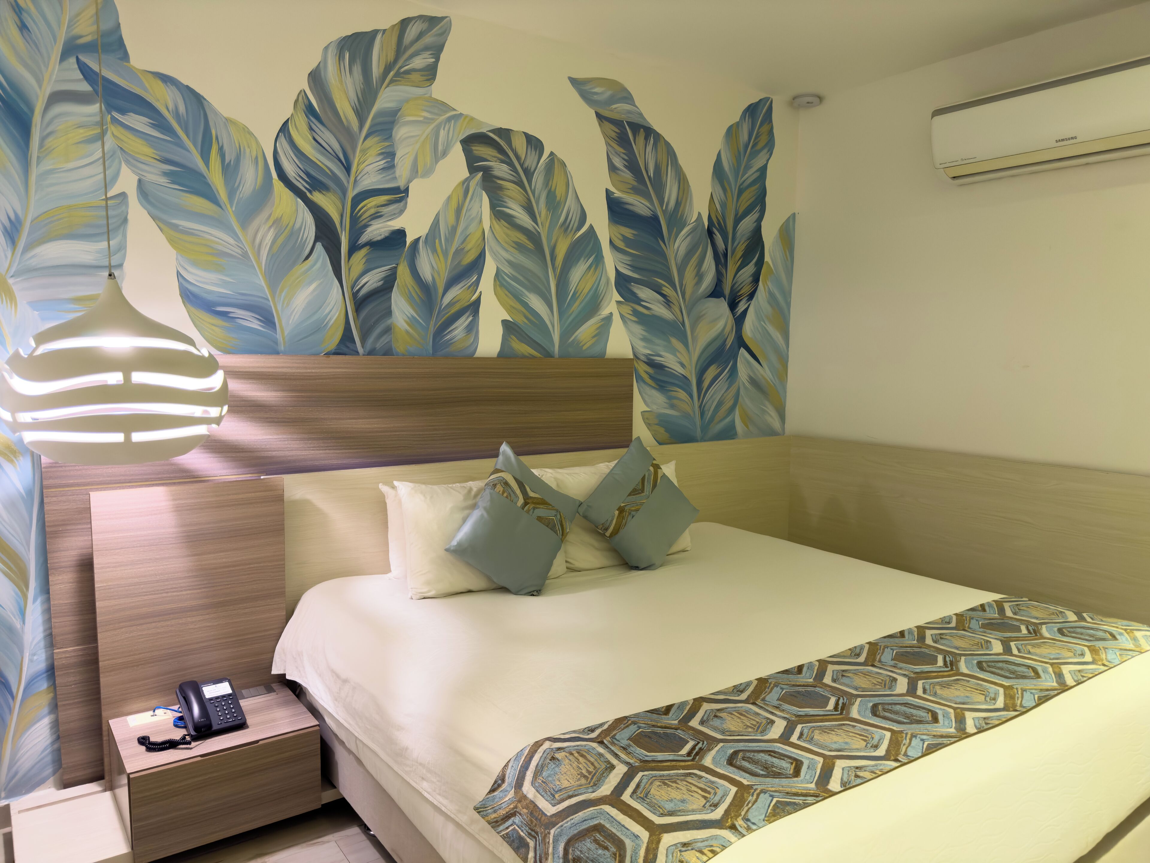A hotel room with a bed, a bedside table with a phone, and a wall with large leaf patterns.