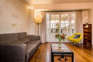 Una sala de estar con un sofá gris, un sillón amarillo, una mesa de centro de madera y vistas al balcón exterior a través de un ventanal.