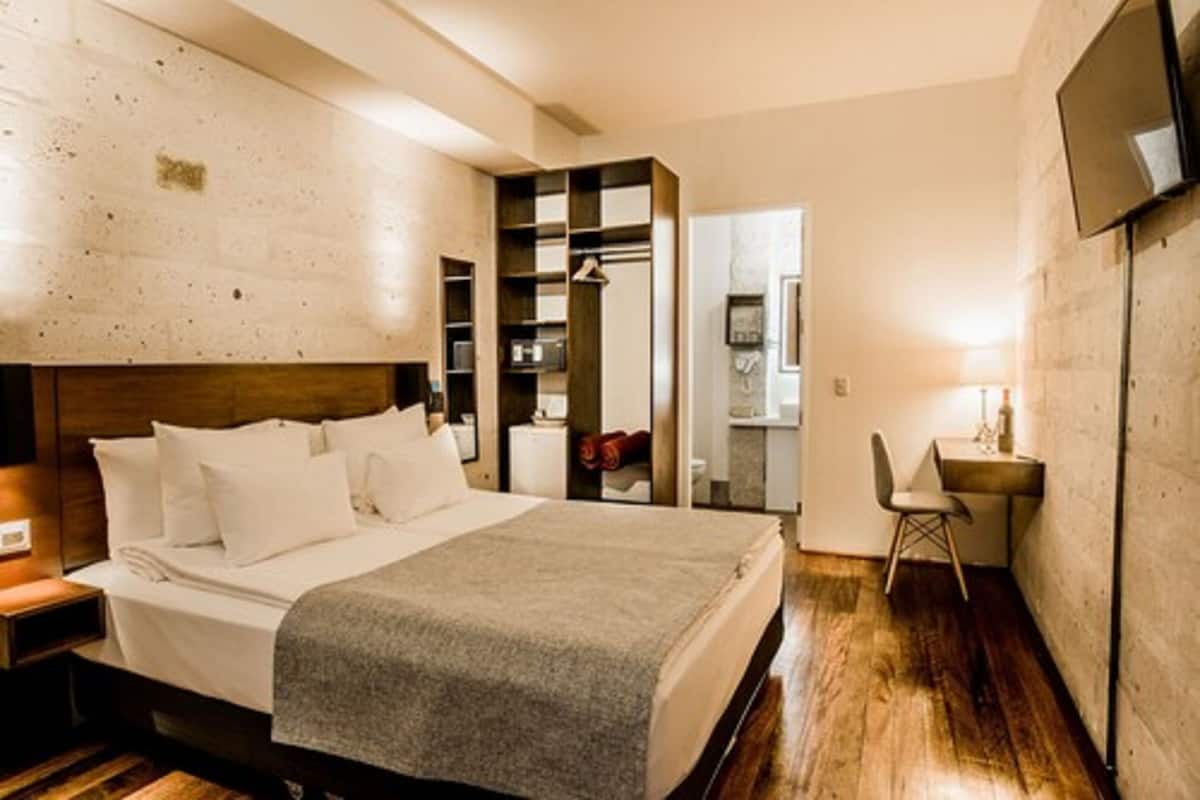 A bedroom with a bed, a desk, and a chair. There is a wardrobe and a mirror.